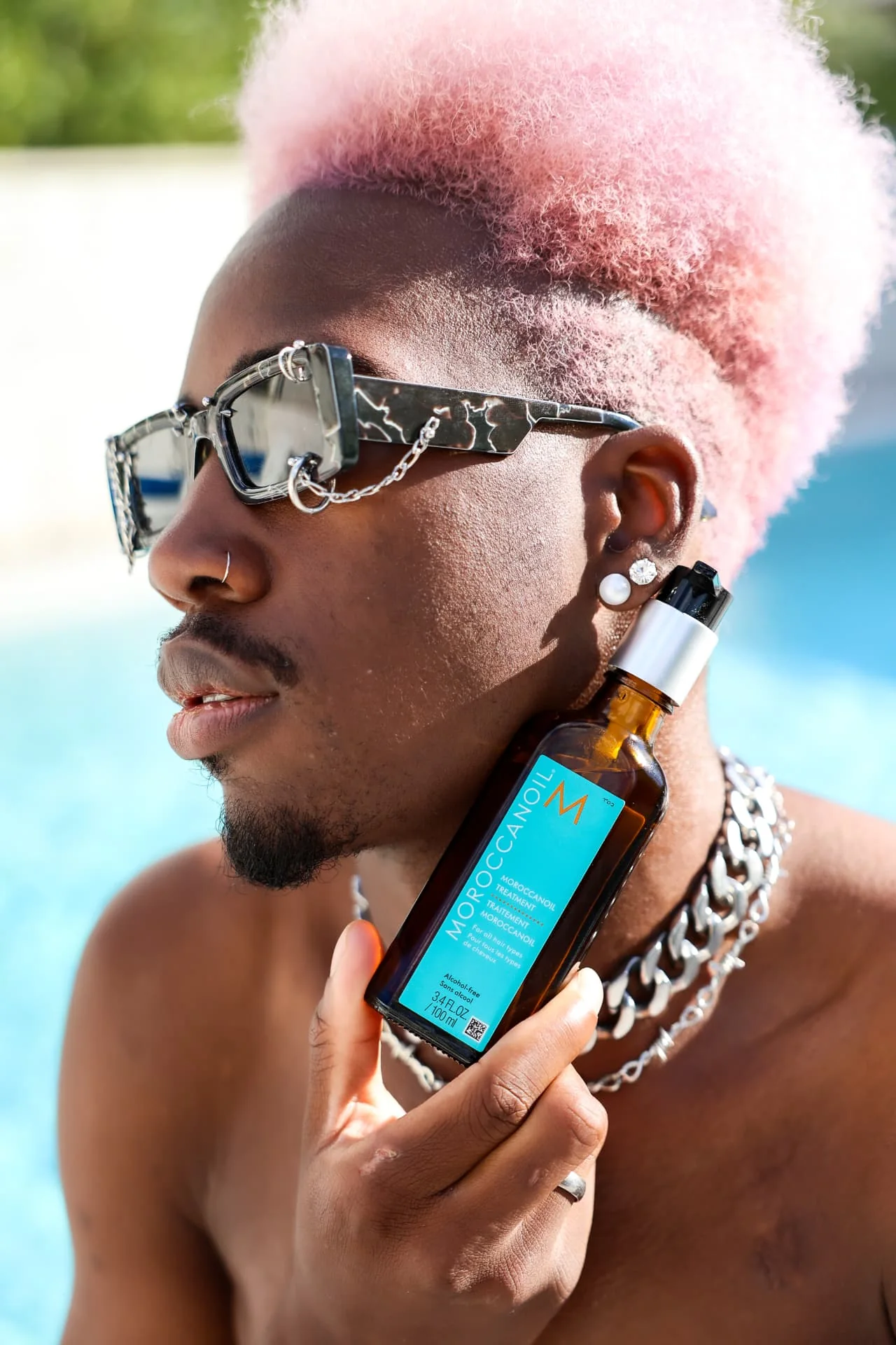 Model s ružičastom kosom drži bocu Moroccanoil Treatment uz bazen