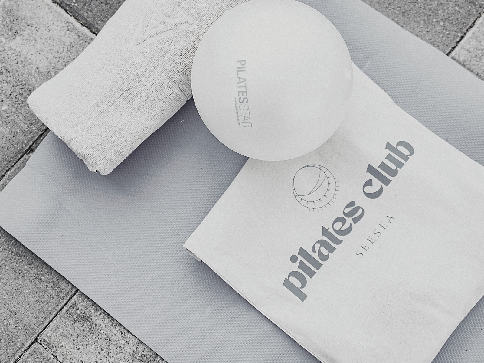 Podloga za vježbanje, lopta za pilates, ručnik i platnena torba na kamenim pločama.